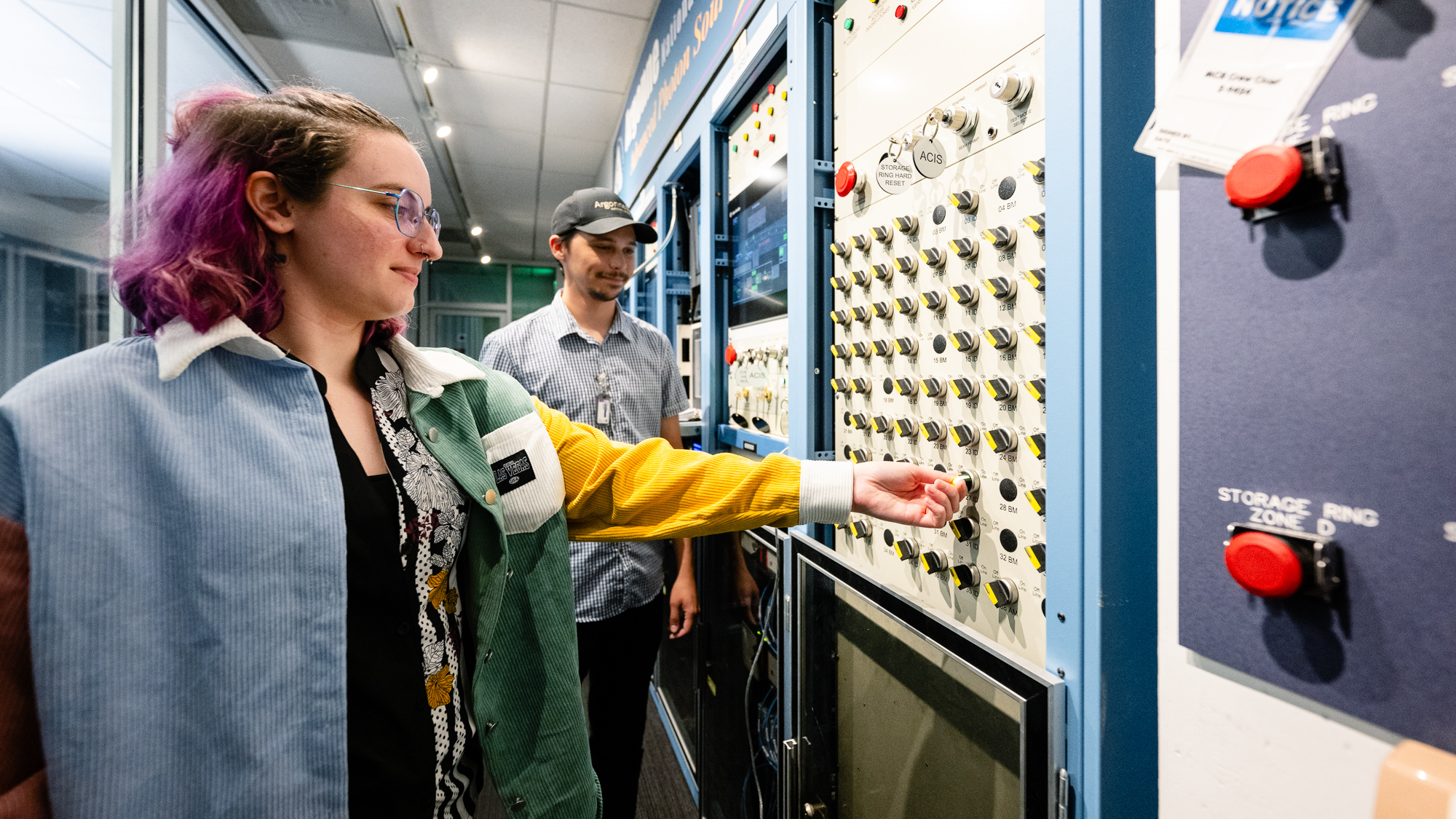 A woman turns a key in a control room while a man look on.