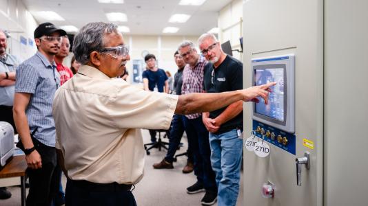 A man presses a button while his colleagues look on with smiles.