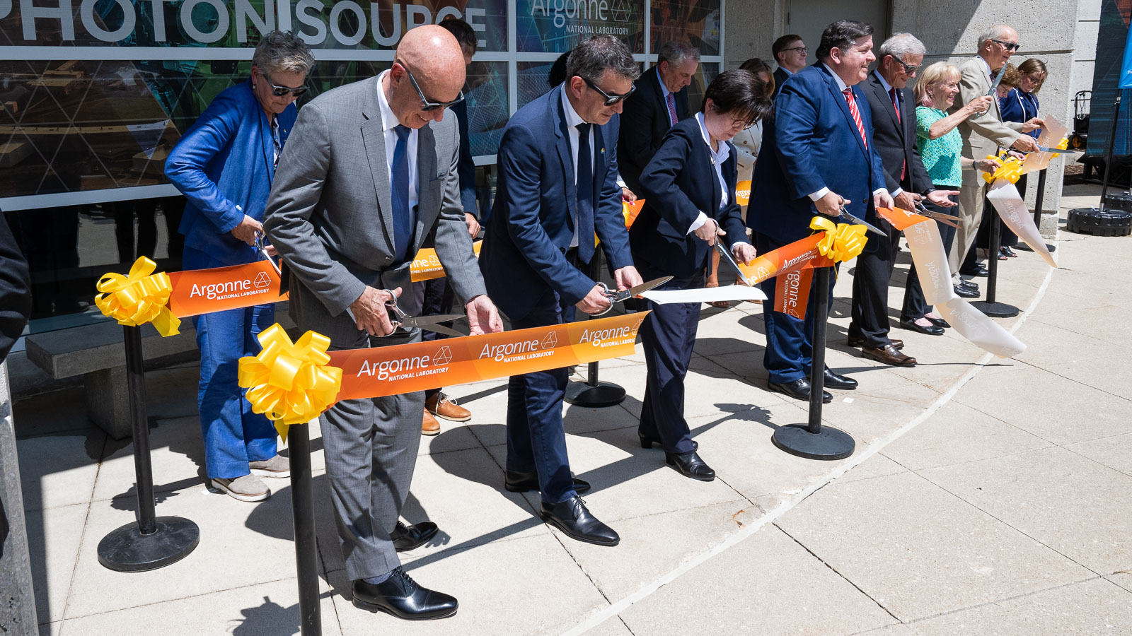 People standing in a row cutting a giant ribbon.