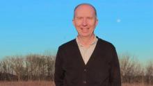 Man in a black sweater standing in a field with trees behind him